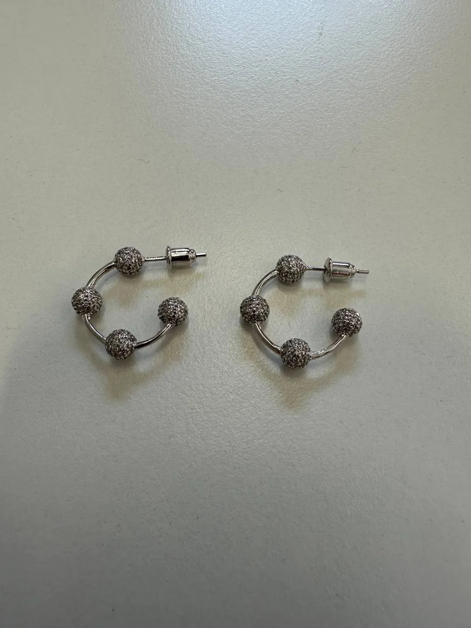 The same earrings shot on a phone on a beige desk