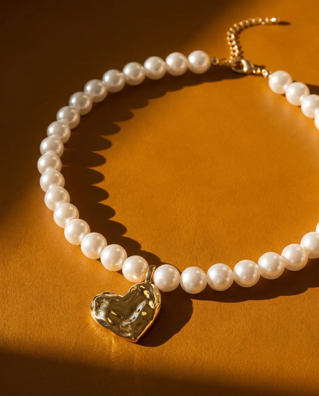 Product shot — a pearl necklace with a gold pendant on a warm surface